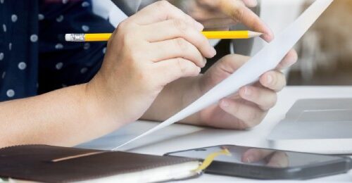 Manos escribiendo en documentos y laptop